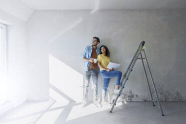 Thoughtful couple standing in front of wall at new home - AAZF01456