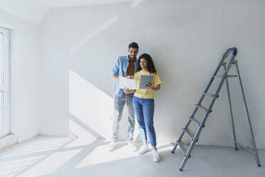 Young couple holding tablet PC and planning with blueprint for renovation in front of wall - AAZF01457