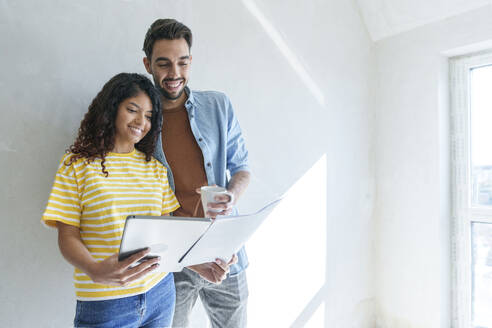 Glückliches Paar mit Tablet-PC, das einen Bauplan für die Renovierung seines neuen Hauses analysiert - AAZF01462