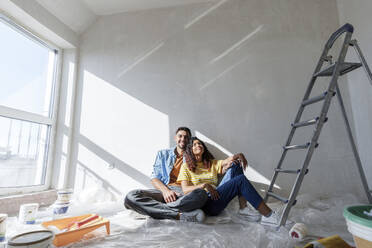 Young couple sitting on floor near wall in room under renovation - AAZF01464