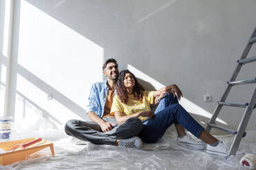 Thoughtful couple sitting near wall at new home - AAZF01465