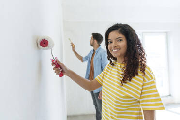 Smiling woman with paint roller standing near man at new home - AAZF01467