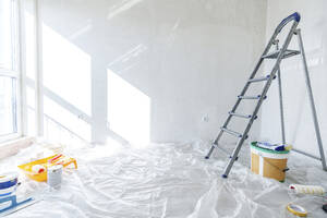 Painting equipment and ladder on floor covered in plastic at home - AAZF01471
