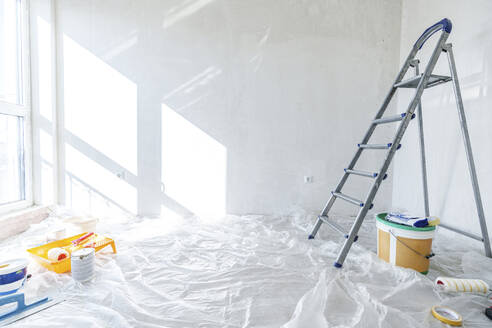 Malerausrüstung und Leiter auf dem mit Plastik abgedeckten Boden zu Hause - AAZF01471