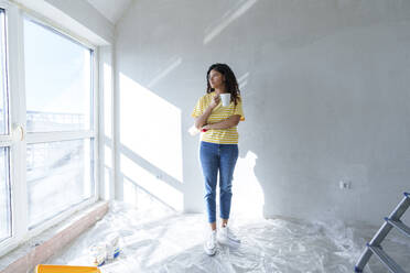 Young woman with coffee cup standing in room under renovation - AAZF01477