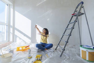 Woman sitting near ladder and planning for renovation in new home - AAZF01480