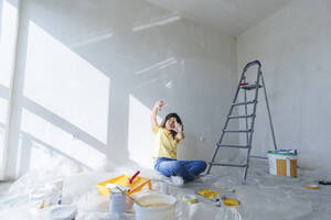 Thoughtful woman sitting on floor and planning for renovation in new home - AAZF01481