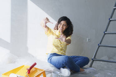 Happy woman gesturing finger frame and planning for renovation in new home - AAZF01482