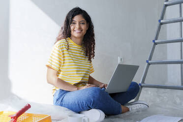 Smiling woman sitting with laptop at new home - AAZF01485