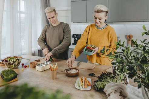 Happy couple preparing healthy food for lunch boxes in kitchen at home - YTF01675