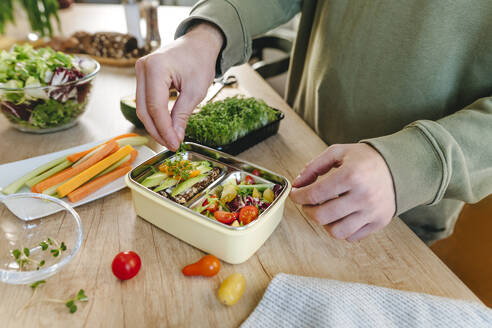 Man garnishing microgreen over vegetarian food in lunch box - YTF01683