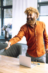 Happy businessman shaking hands with colleague at desk - JOSEF23299