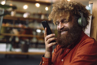 Glücklicher Geschäftsmann mit drahtlosen Kopfhörern, der Musik hört und sein Smartphone in der Hand hält - JOSEF23303