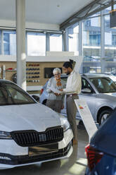 Verkäufer, der mit einem Kunden über ein Dokument in einem Autohaus diskutiert - IKF01582
