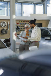 Salesperson discussing with woman over document in car showroom - IKF01583