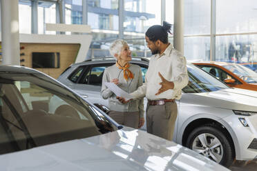 Salesperson discussing with smiling customer in car showroom - IKF01584