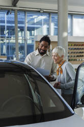 Happy salesperson showing car to customer in showroom - IKF01589