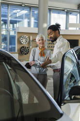 Smiling salesperson showing car to customer in showroom - IKF01592