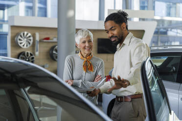 Happy salesperson showing car to customer in showroom - IKF01593