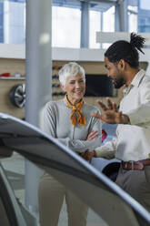 Salesperson showing car to happy customer in showroom - IKF01594