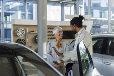 Salesperson discussing over car to happy customer in showroom - IKF01595