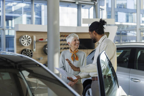 Verkäufer bei der Besprechung eines Autos mit einem zufriedenen Kunden im Ausstellungsraum - IKF01595