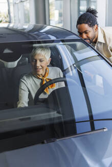 Smiling salesperson with customer examining car in showroom - IKF01600