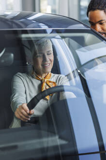 Salesperson with smiling customer examining car in showroom - IKF01601