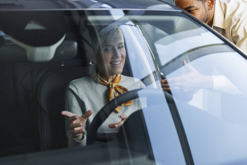 Salesperson with happy senior woman examining car in showroom - IKF01602