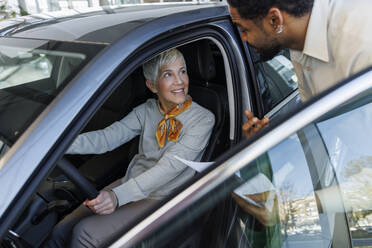 Salesperson discussing with smiling customer sitting in car - IKF01604