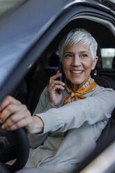 Lächelnde ältere Frau, die im Auto mit ihrem Smartphone telefoniert - IKF01608