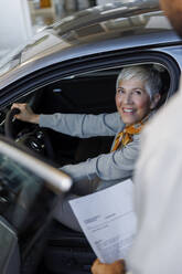 Smiling woman with salesperson holding document in car showroom - IKF01609