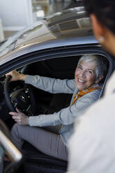 Happy woman sitting in car near salesperson in showroom - IKF01610