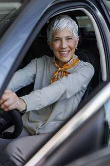 Glückliche ältere Frau sitzt im Auto im Ausstellungsraum - IKF01615