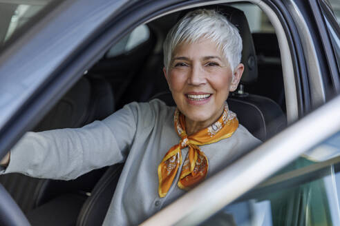 Glückliche ältere Frau mit grauem Haar sitzt im Auto - IKF01616