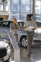 Salesperson walking and having discussion with customer in car showroom - IKF01617