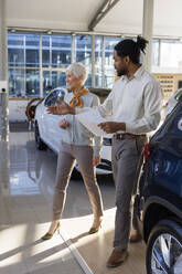 Smiling salesperson having discussion with customer in car showroom - IKF01618