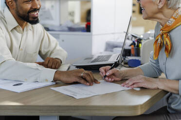 Happy salesperson with customer doing paperwork at desk - IKF01628