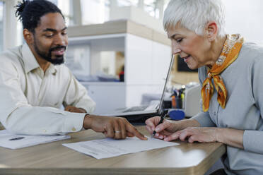 Salesperson explaining to customer doing paperwork at desk - IKF01630