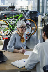 Senior woman talking to salesperson at desk - IKF01640