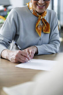 Lächelnde ältere Frau beim Unterzeichnen eines Kaufvertrags am Schreibtisch - IKF01645