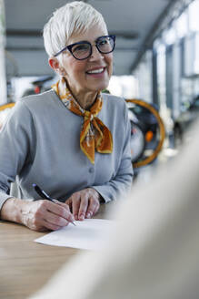 Happy senior woman doing paperwork at desk - IKF01646