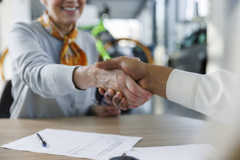 Smiling woman shaking hands with car salesperson at desk - IKF01649