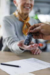 Hand eines Verkäufers, der einer am Schreibtisch sitzenden Frau die Autoschlüssel gibt - IKF01653