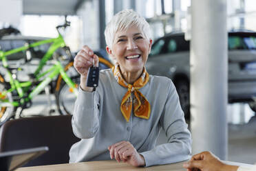 Happy senior woman holding car keys in showroom - IKF01657