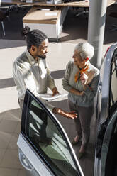 Happy senior woman with salesperson showing car at showroom - IKF01662