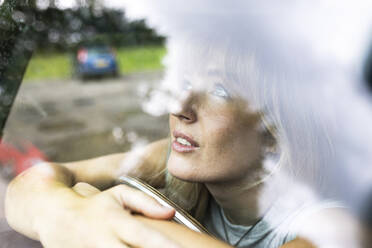 Smiling young beautiful woman looking through car window - WPEF08257