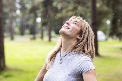 Smiling woman enjoying rain in forest - WPEF08270