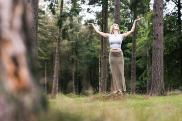 Frau steht mit erhobenen Armen vor Bäumen - WPEF08281