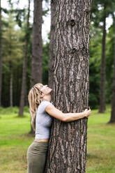Young beautiful woman hugging tree in forest - WPEF08285